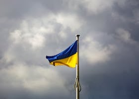 A Ukrainian flag waves prominently against a dramatic cloudy sky, symbolizing resilience.