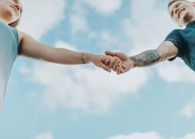 A couple holds hands outdoors, symbolizing love and connection, photographed from a low angle.
