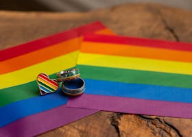 Close-up of rainbow rings and heart pin on a pride flag, symbolic of LGBTQ pride and love.